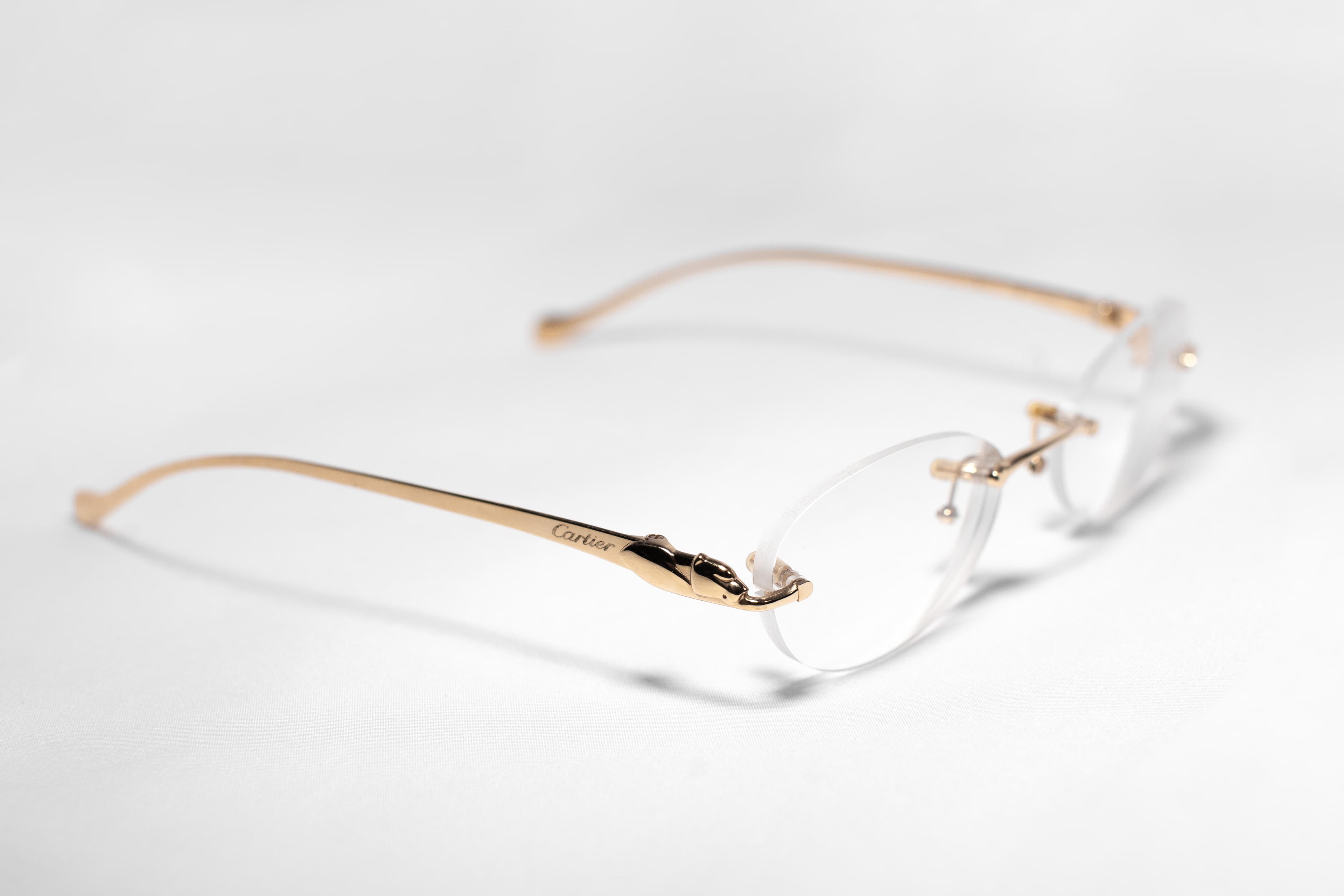 Gold rimless eyeglass frame on a soft white surface, side view with shallow depth of field.