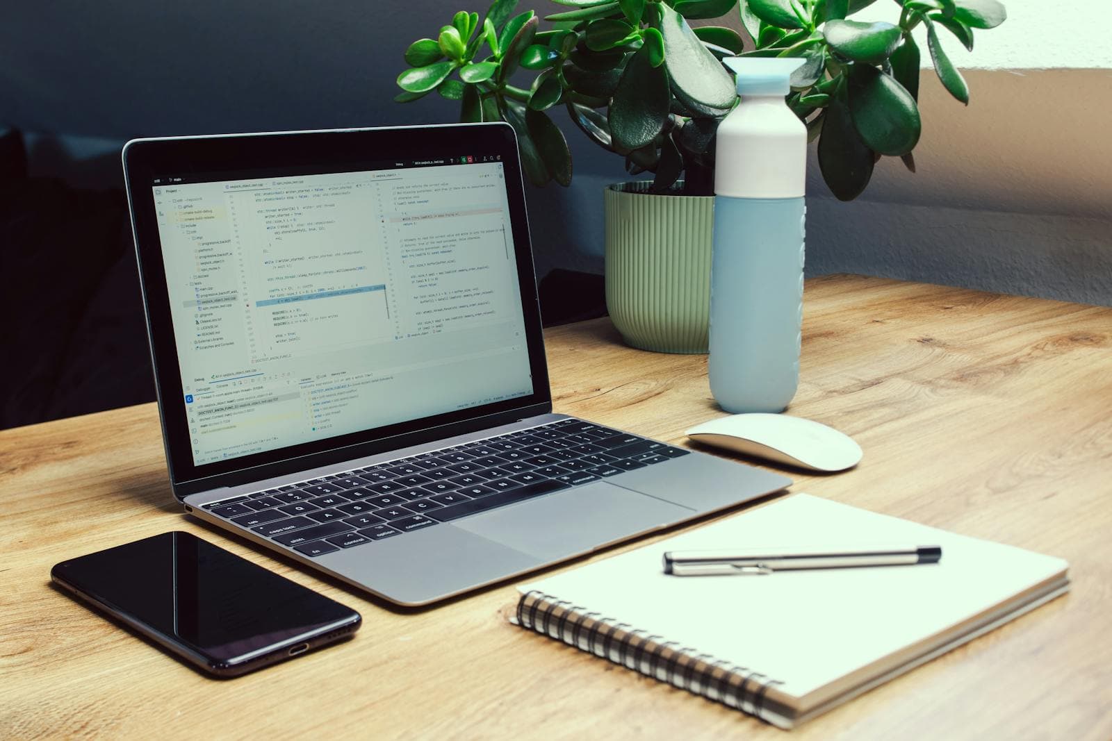 Workspace with a laptop, coffee, notebook, and pens in soft window light.