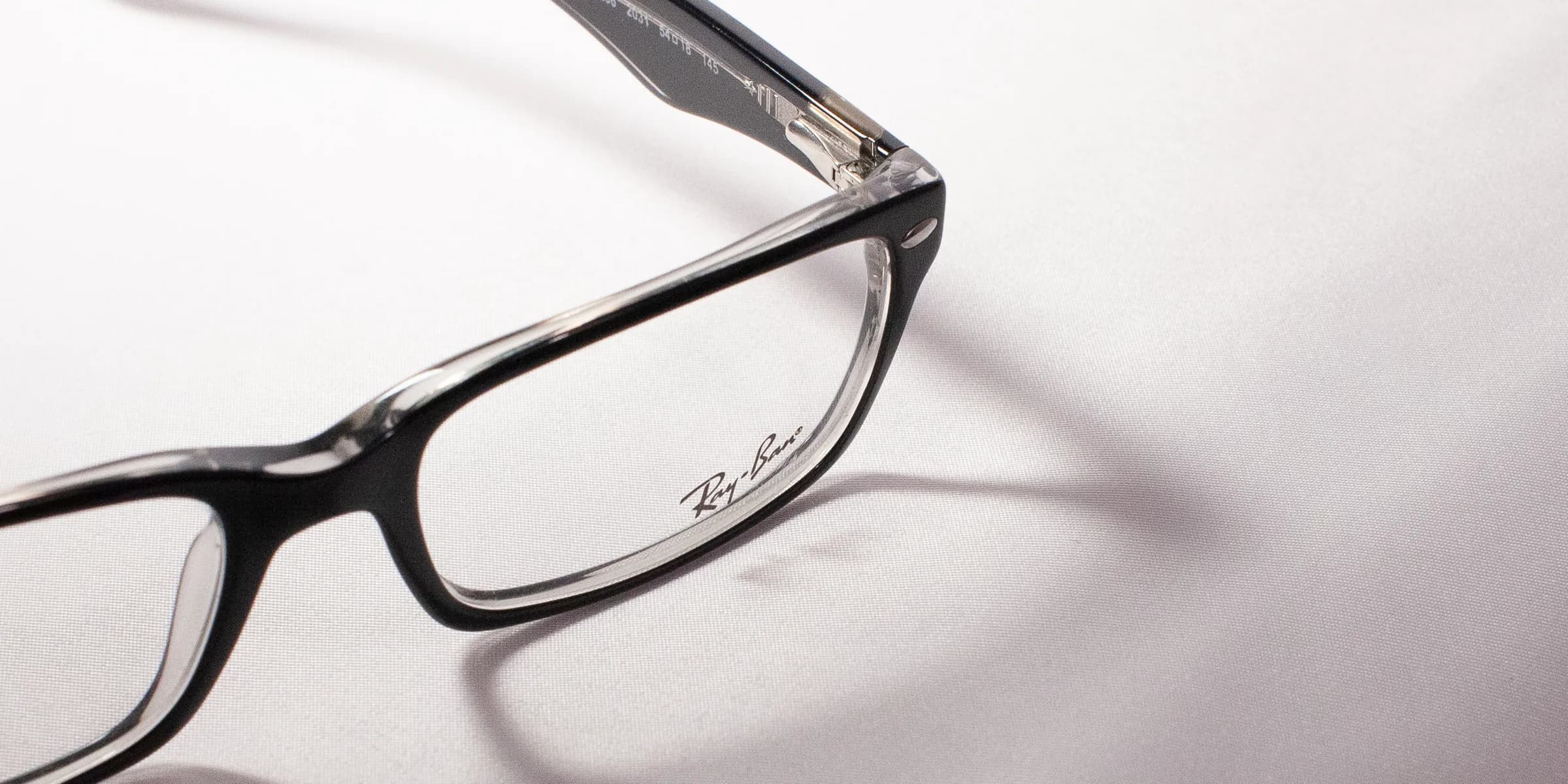 Close-up of a black Ray-Ban optical frame at a low angle, the temple signature in focus.